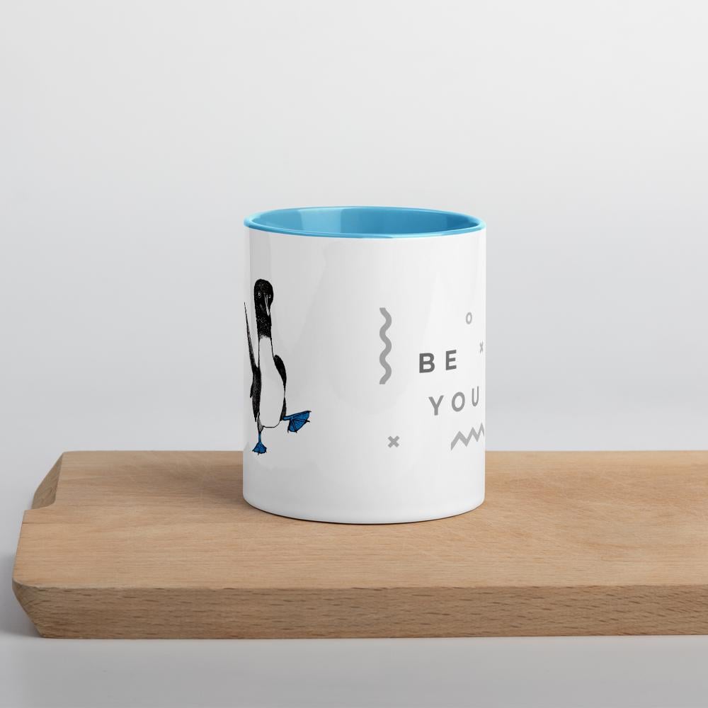 Light blue ceramic mug with Be You in bold text above a detailed illustration of a blue-footed booby. Features fine textures and lifelike details. Glossy finish with a standard-sized handle.