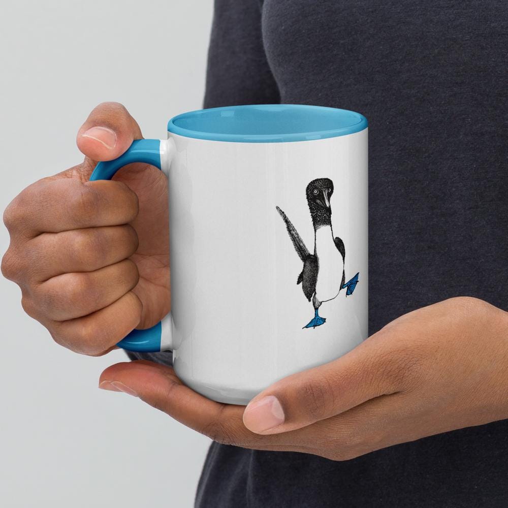 Light blue ceramic mug with Be You in bold text above a detailed illustration of a blue-footed booby. Features fine textures and lifelike details. Glossy finish with a standard-sized handle.